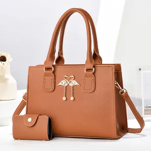 Detalle de bolso tote marrón con colgante de cisne, perlas y herrajes dorados