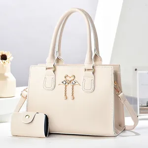 Detalle de bolso beige en cuero lichi con hebilla de cisne metálica y borla de perlas