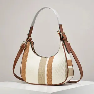 Detailed side view of striped woven crescent bag with brown leather trim and gold hardware