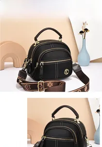 Detail of black pebbled leather bag with triple zipper pockets and wide floral strap
