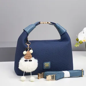 Detail of navy blue canvas texture bag with golden logo and cute plush charm accessory