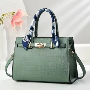 Détail d'un sac à main vert clair motif crocodile avec foulard et fermoir doré chic