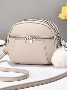 Minimalist beige pebble leather crossbody bag with triple zippers and pompom charm