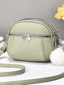Sage green lychee leather mini crossbody bag with three zippers and a plush pompom