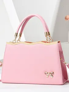 Pink crossbody handbag with metallic wavy trim and a decorative gold bow accessory
