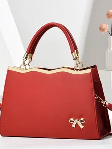 Red saffiano leather tote bag with gold metal trim and bow accent on a white stand