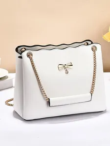 Elegant white shoulder bag with black trim and gold bow metal detail in a studio setting