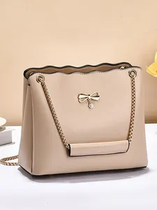 Elegant beige crossbody bag with golden bow hardware and chain strap in minimalist indoor setting