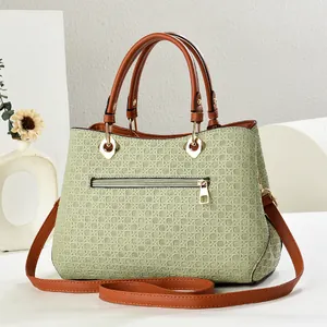 Detail of woven texture on green shoulder bag with brown leather handle and gold hardware