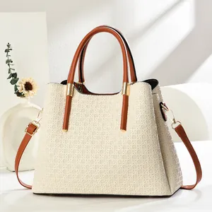 Close-up of beige woven texture handbag with brown leather handles and gold metal hardware