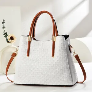 Detail of white geometric woven handbag with brown leather strap and gold hardware