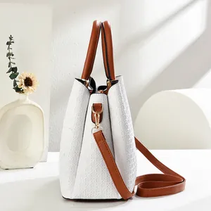 Detail of white textured handbag with brown leather trim and golden metal hardware