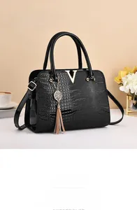Detail of crocodile embossed leather handbag with gold V-shaped logo and elegant fringe tassel