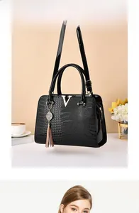 Detail of black crocodile embossed handbag featuring a metal V-logo and tassel charm