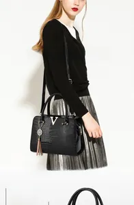 Close-up of black crocodile pattern leather handbag with gold V-logo and tassel detail