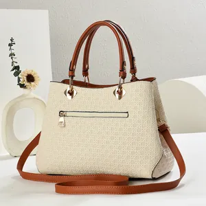 Detail of woven texture and gold hardware on a cream shoulder bag with brown handles
