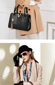 Detail of black crocodile texture handbag with golden V buckle and tassel accessory