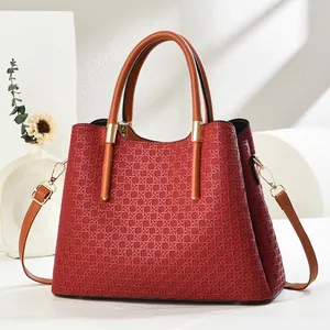 Detail of red trapezoid handbag with embossed weave texture and brown handles