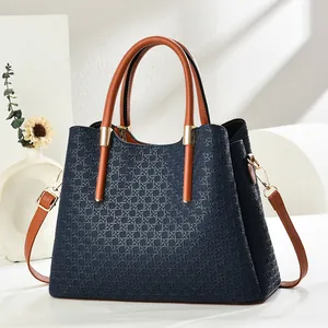 Detail of navy blue tote bag with 3D weave texture, brown handles and gold hardware