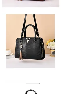 Detail of black glossy crocodile embossed handbag with golden V logo and tan tassel charm