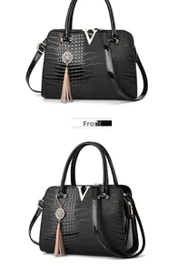 Detailed front view of black crocodile embossed handbag with golden V buckle and tassel