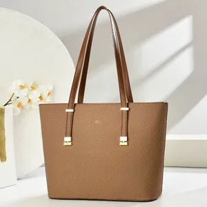 Detail of a brown tote bag with fine texture, golden hardware and slim shoulder straps