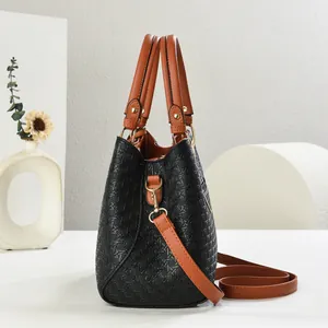 Detail of woven texture black tote with brown leather handles and gold metal hardware