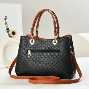 Close-up of woven texture black tote bag with brown leather handles and gold hardware
