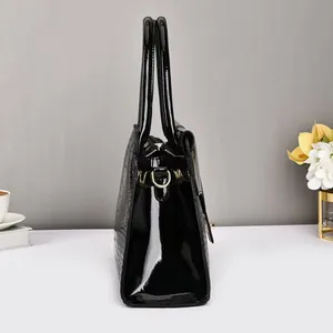 Detail view of the black glossy faux crocodile texture and gold hardware on the handbag