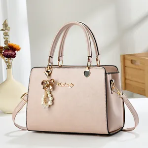 Detail of light pink textured leather bag with pearl bow charm and gold-toned brand logo