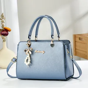 Detail showing light blue cross-grain leather texture with pearl bow pendant and metal logo