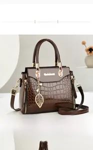Detail of dark brown faux-crocodile handbag with gold hardware and leaf pendant charm