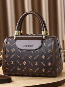 Brown textured Boston handbag with MQCKDE print and golden hardware on wooden surface
