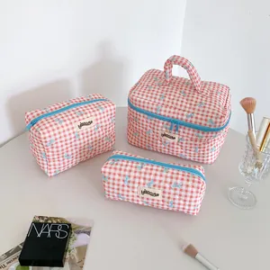 Detailed set of three red checkered makeup bags with light blue bow patterns on a desk