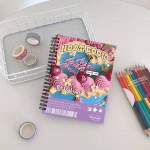 Detail of a spiral notebook featuring a cute cream cake design on a white desktop