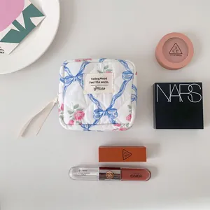 Quilted floral cosmetic bag with blue ribbons and zipper detail on white background