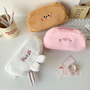 Detailed view of three plush animal pencil cases in brown, pink, and white on a desk