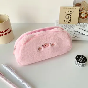 Close-up of pink plush pig pencil case with embroidery details on a minimalist desk