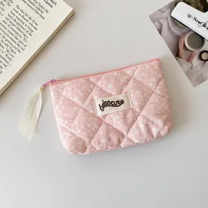 Detalle de bolsa acolchada rosa con flores, logotipo de lona y cinta de cremallera