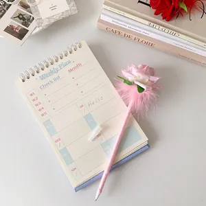 Close-up of pink rose feather pen and spiral weekly planner on a white desk
