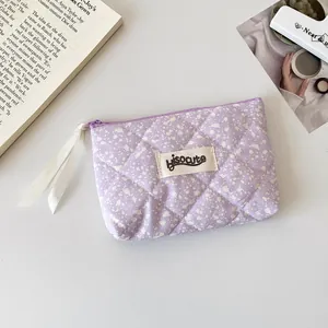 Detalle del estuche de tela acolchada lavanda con salpicaduras de tinta y etiqueta logo