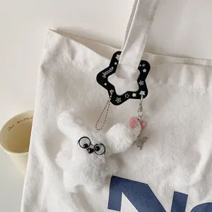 White plush bunny keychain with star carabiner and butterfly charm on canvas bag