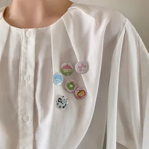 Close-up of cute cartoon tinplate badges pinned on a white textured shirt for decoration