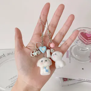 Hand holding two cute white flocked puppy charms with blue heart and bone accessories