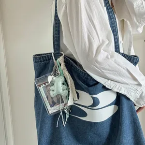 Detail of denim tote bag with plush bear keychain and heart pendant on shoulder strap