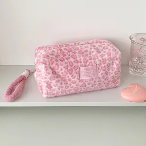 Detail showing plush pink leopard print makeup bag with fuzzy handle and stitched logo tag