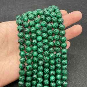Primo piano di perline tonde in malachite verde con trama naturale striata in mano