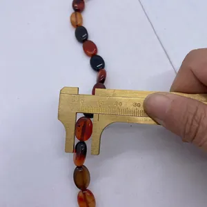 Messen der 10mm Breite einer ovalen roten Achat-Flachperle mit einem goldenen Messschieber