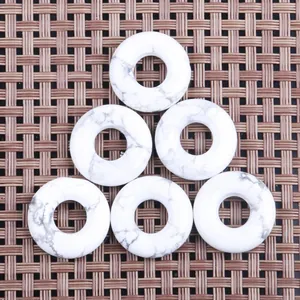 Macro detail of six white howlite stone donut pendants with natural grey veins on a woven mat