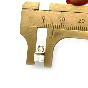 Macro view of a 10mm white turquoise cube pendant measured with a brass caliper